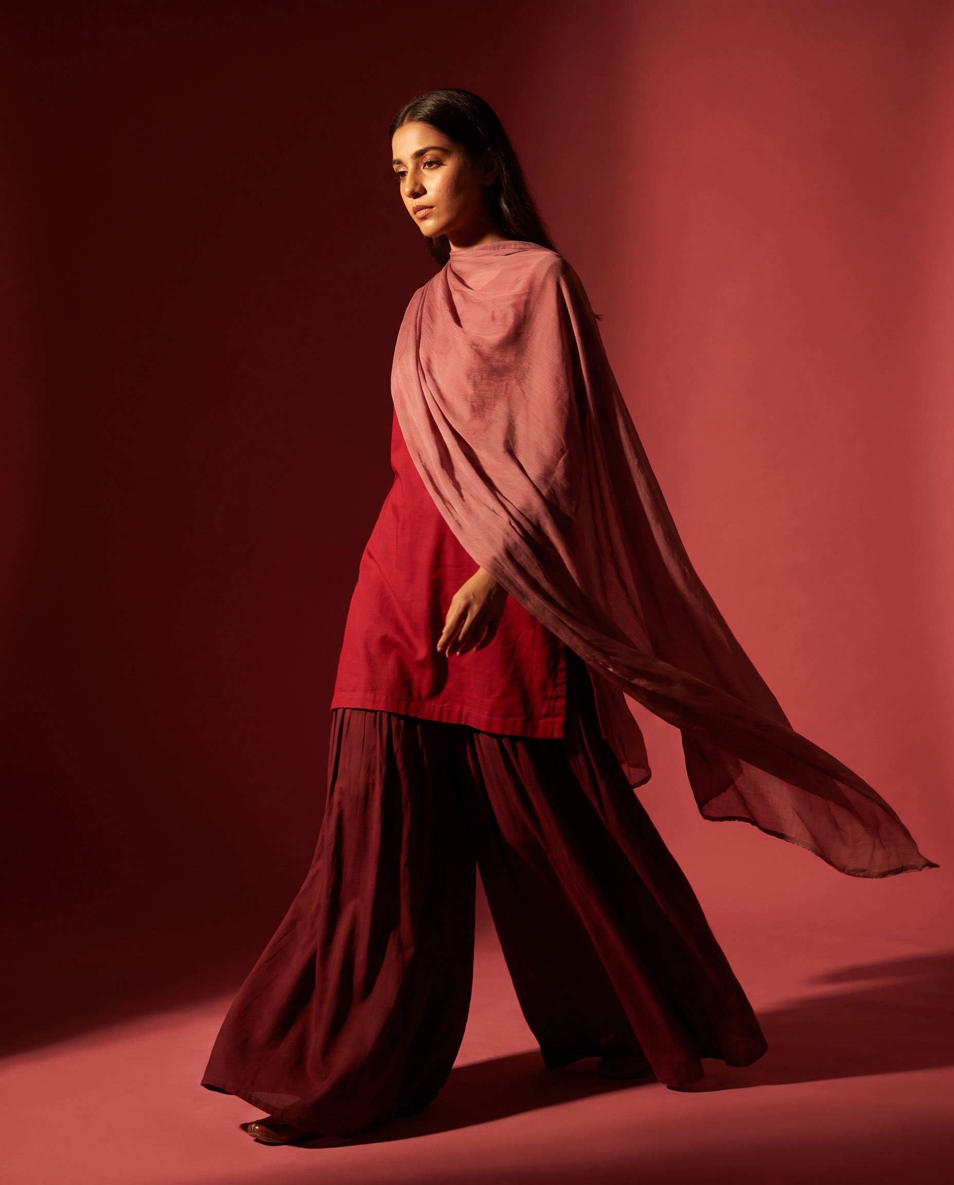 Model walking in a maroon farshi shalwar set, fabric sweeping the floor